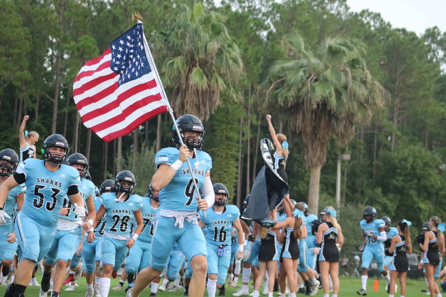 Luke Pirris leads the Sharks onto the football field while carrying an American flag.